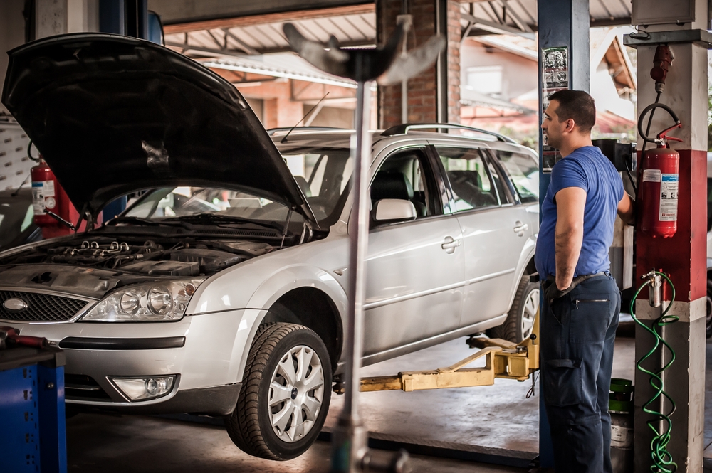 Car mechanic working in a repair garage with hydraulic car lift.